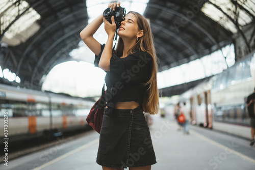 A young girl is a tourist who visits different cities and takes photos of different urban views. At the railway station, a nice young lady with a camera in her hands takes pictures
