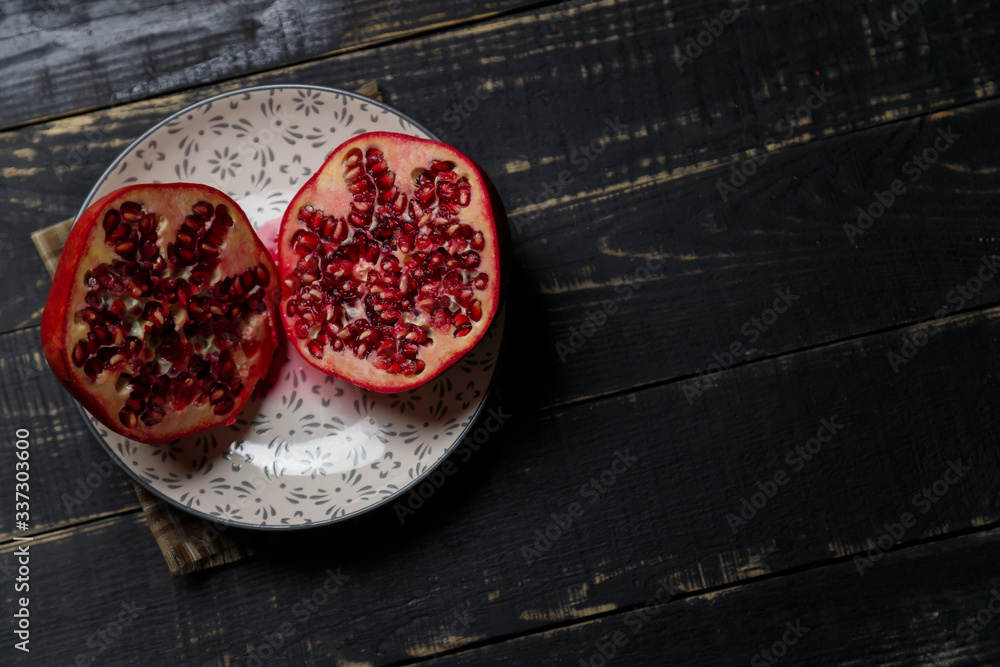 Two halves of pomegranate fruit on plate on black wooden background. Copy space