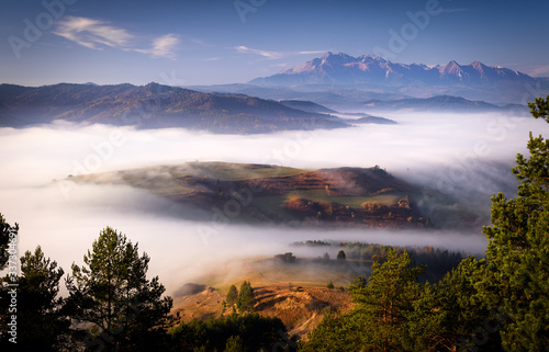 Beautiful, colorful autumn panorama of Pieniny Mountains (Male Pieniny) in the fog and morning light with Tatra Mountains in the background. Poland, Slovakia.
