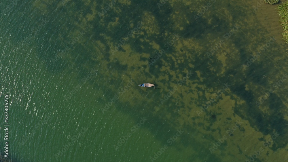 Aerial top down view of long tail boat floating on Thu Bon river. Green color water. Beautiful landscape from drone. Water plants under water surface. Hoi An, Vietnam Aerial top down view of long tail boat floating on Thu Bon river. Green color water. Beautiful landscape from drone. Water plants under water surface. Hoi An, Vietnam