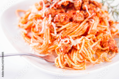 Spaghetti bolognese on a plate sprinkled with cheese eaten with a fork