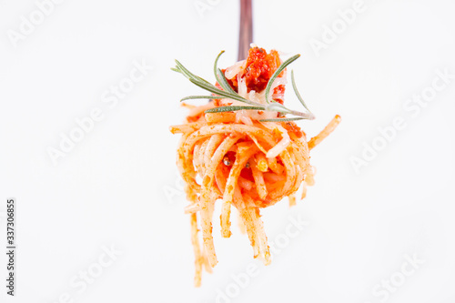 Spaghetti bolognese sprinkled with cheese and decorated with a rosemary twig on a fork on a white background