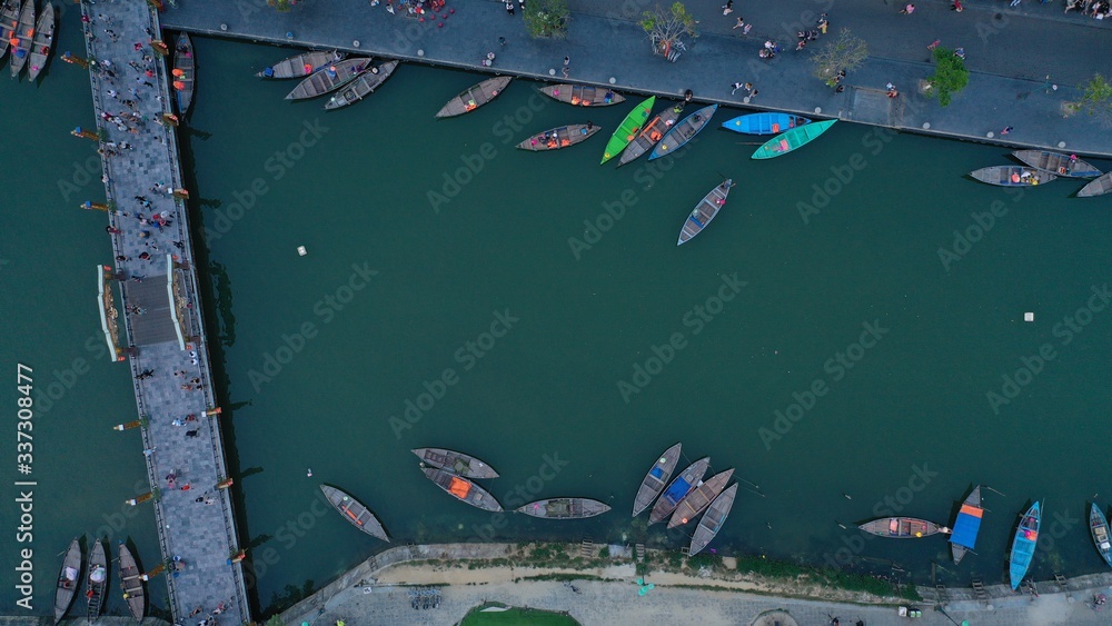 Aerial top down view of colourful long tail boats moored to embankment on Thu Bon river near bridge, Hoi An ancient town, Quang Nam province, Vietnam. Popular travel destination.