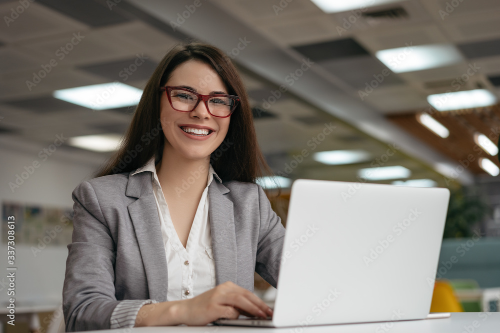 Portrait of insurance agent using laptop computer, working at workplace. Successful business woman looking at camera and smiling, sitting in modern office Portrait of insurance agent using laptop computer, working at workplace. Successful business woman looking at camera and smiling, sitting in modern office