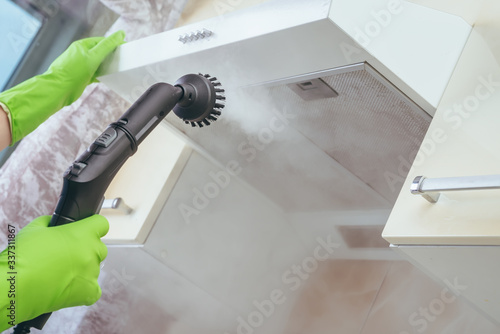 house cleaning. Girl brushes steam cleaners kitchen drawing with steam in green gloves. cleaning of a surface. photo