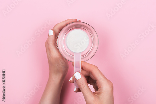 Woman hands with a scoop with collagen or protein powder and a glass of water. Trendy beauty supplement for healthy skin and bones. Flatlay, top view.
