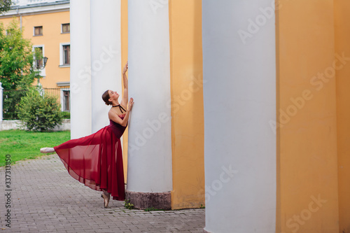 Woman ballerina in red ballet dress dancing in pointe shoes next to the old columns