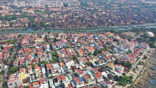 Aerial view of Hoi An old town on Thu Bon river, Quang Nam province, Vietnam. Unesco world heritage. Boats moored to river embankment. Bridge. Many roof tops.