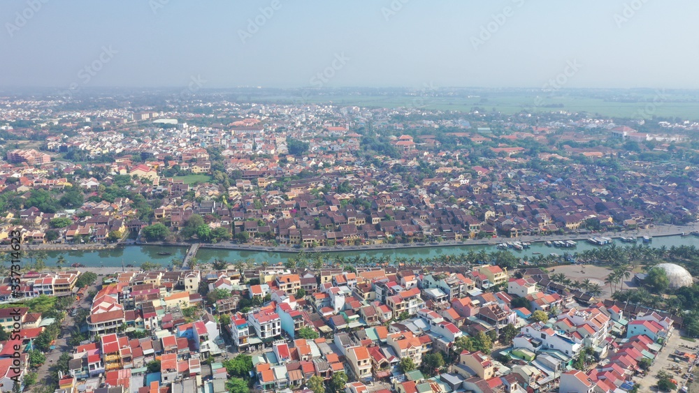 Aerial view of Hoi An old town on Thu Bon river, Quang Nam province, Vietnam. Unesco world heritage. Boats moored to river embankment. Bridge. Many roof tops.