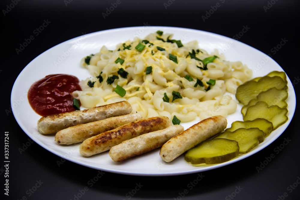 Pasta on a plate with cheese on top and green onions. Delicious pasta made from high quality flour with chicken sausage from grill and sliced cucumber from jar. Horns made of flour cooked with cheese Pasta on a plate with cheese on top and green onions. Delicious pasta made from high quality flour with chicken sausage from grill and sliced cucumber from jar. Horns made of flour cooked with cheese