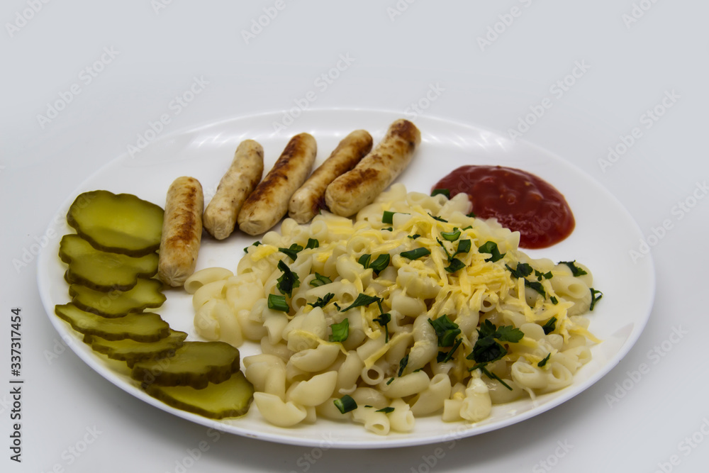 Pasta on a plate with cheese on top and green onions. Delicious pasta made from high quality flour with chicken sausage from grill and sliced cucumber from jar. Horns made of flour cooked with cheese Pasta on a plate with cheese on top and green onions. Delicious pasta made from high quality flour with chicken sausage from grill and sliced cucumber from jar. Horns made of flour cooked with cheese