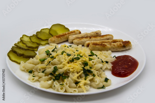 Pasta on a plate with cheese on top and green onions. Delicious pasta made from high quality flour with chicken sausage from grill and sliced cucumber from jar. Horns made of flour cooked with cheese