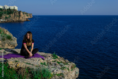 Beautiful young happy girl smiling sitting on rock near sea on a sunny day © Alona Gryadovaya