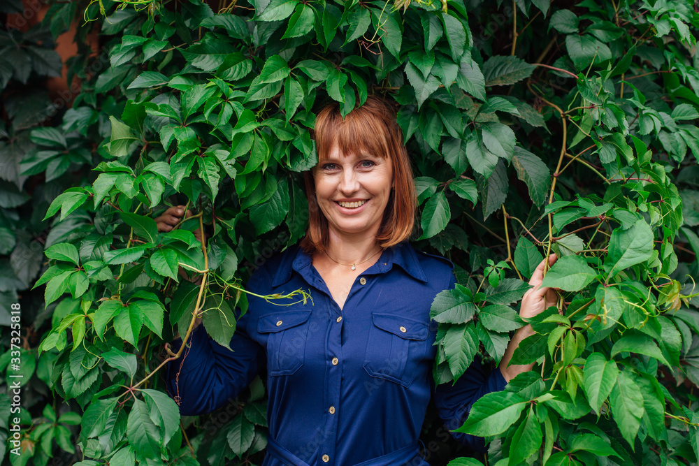 Portrait of a beautiful middle aged woman, standing next to the wall of wild grape leaves. Portrait of a beautiful middle aged woman, standing next to the wall of wild grape leaves.