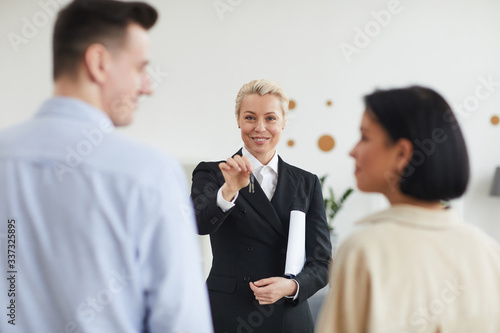 Successful realtor in black suit giving the keys to young couple they buying a new house