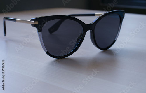 darkened cat-shaped sunglasses lie on the light wooden surface of the table. Elegant, fashionable women's accessory. Reflection of the shadow, place for text. Vacation, summer, vacation photo