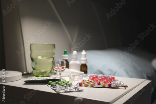 Medicines  medicines  tablets  nose drops  napkins and a glass of water on the bedside table in modern apartments. Concept of home treatment of coronavirus.