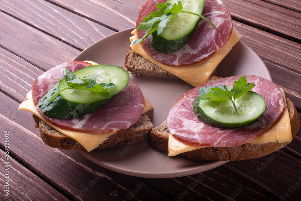 Sandwiches with meat and cheese and green cucumber on a wooden background Sandwiches with meat and cheese and green cucumber on a wooden background