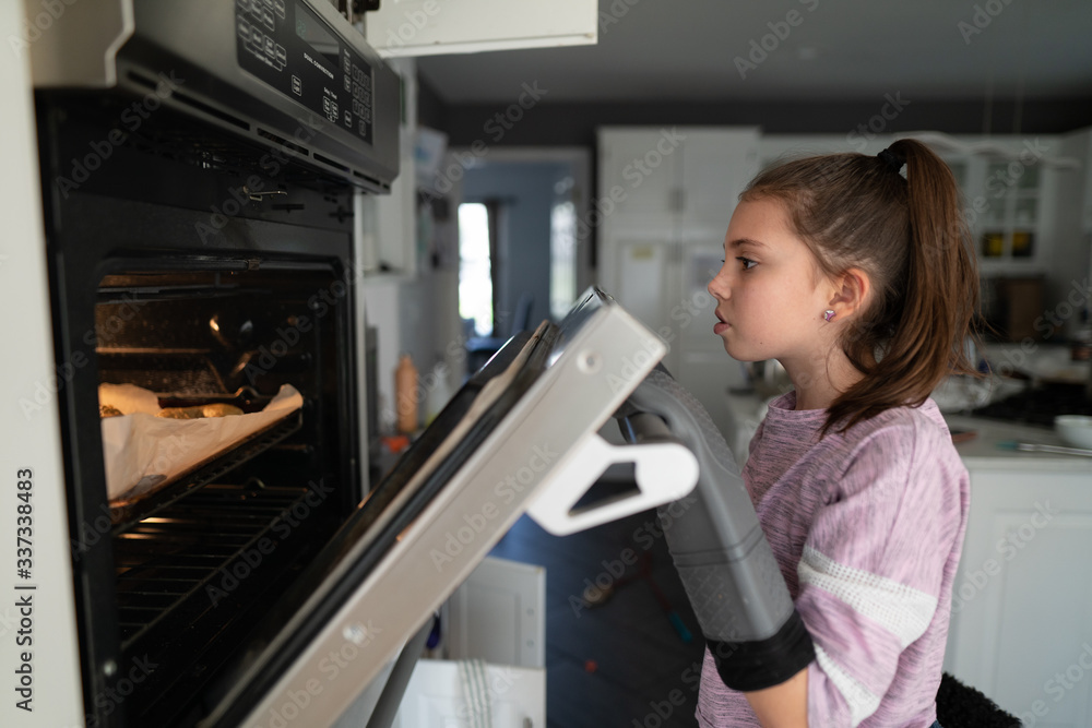 Young girl looking into an oven wearing oven mitts Young girl looking into an oven wearing oven mitts