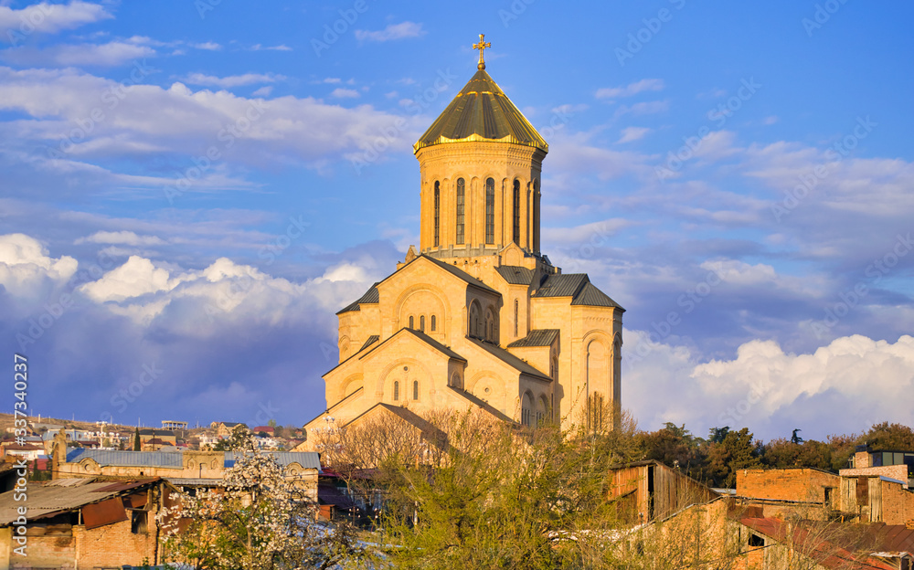 Orthdodox holy trinity church in Tbilisi with many hosues around and blooming spring trees. Religion and culture of Kartvelians. Sakartvelo.