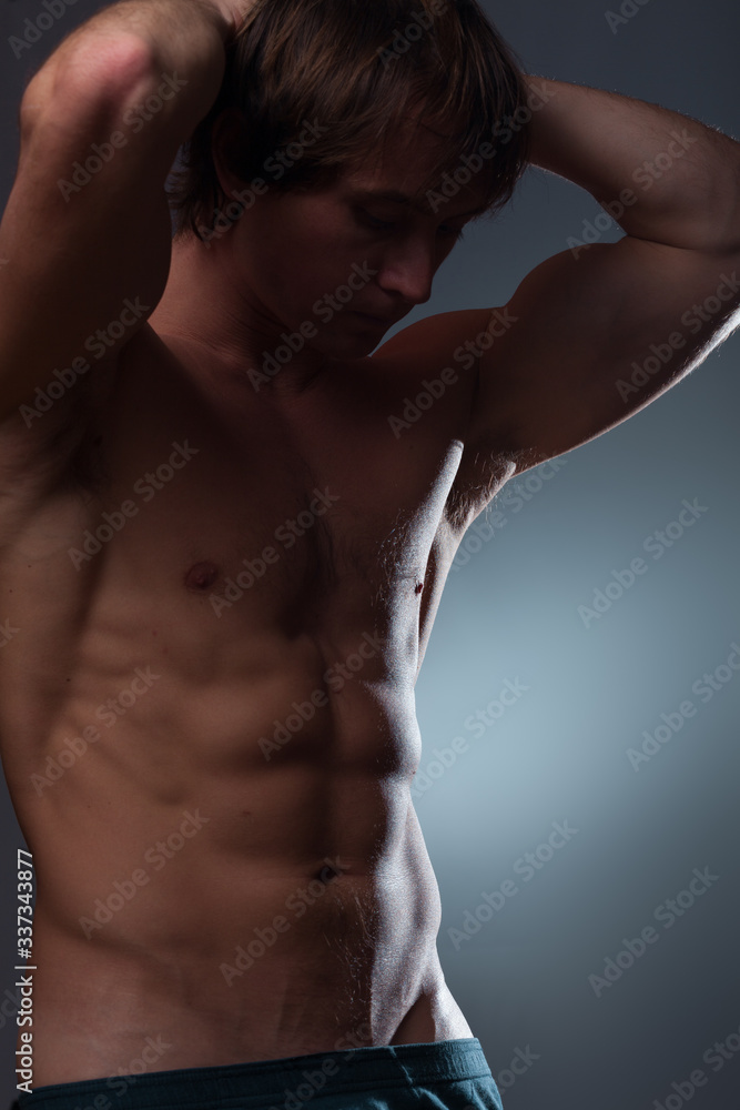 Naklejka premium Young bodybuilder with naturally looking body (hairs and birthmarks) on a gray background