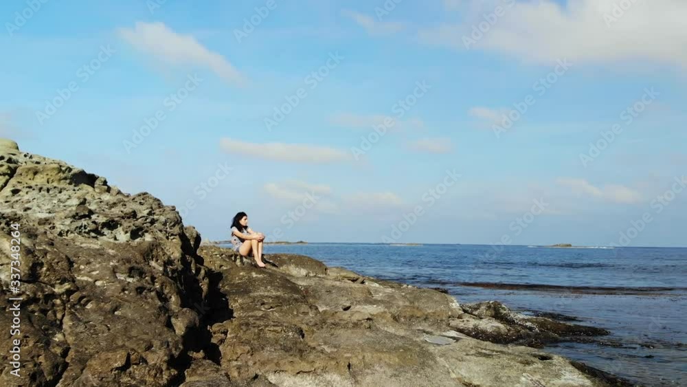Dolly forward revealing a young girl sitting alone on a rocky beach Dolly forward revealing a young girl sitting alone on a rocky beach