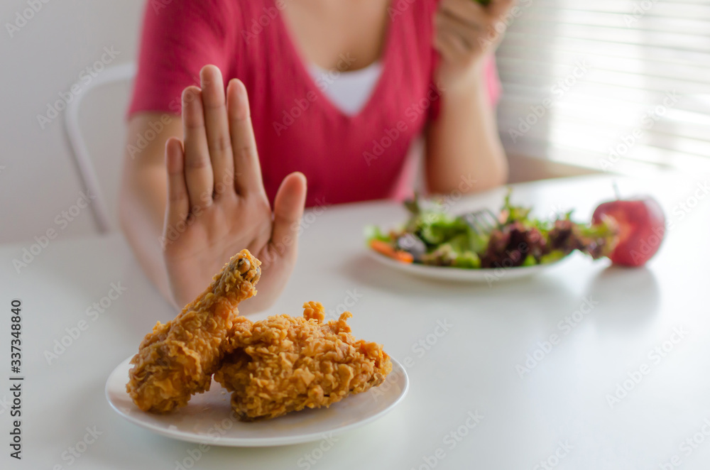 delicious hot fried chicken on dish and woman eating fresh vegetables salad an apple on desk for good health at home, weight loss, junk food , healthy lifestyle, healthy food and dieting plan concept delicious hot fried chicken on dish and woman eating fresh vegetables salad an apple on desk for good health at home, weight loss, junk food , healthy lifestyle, healthy food and dieting plan concept