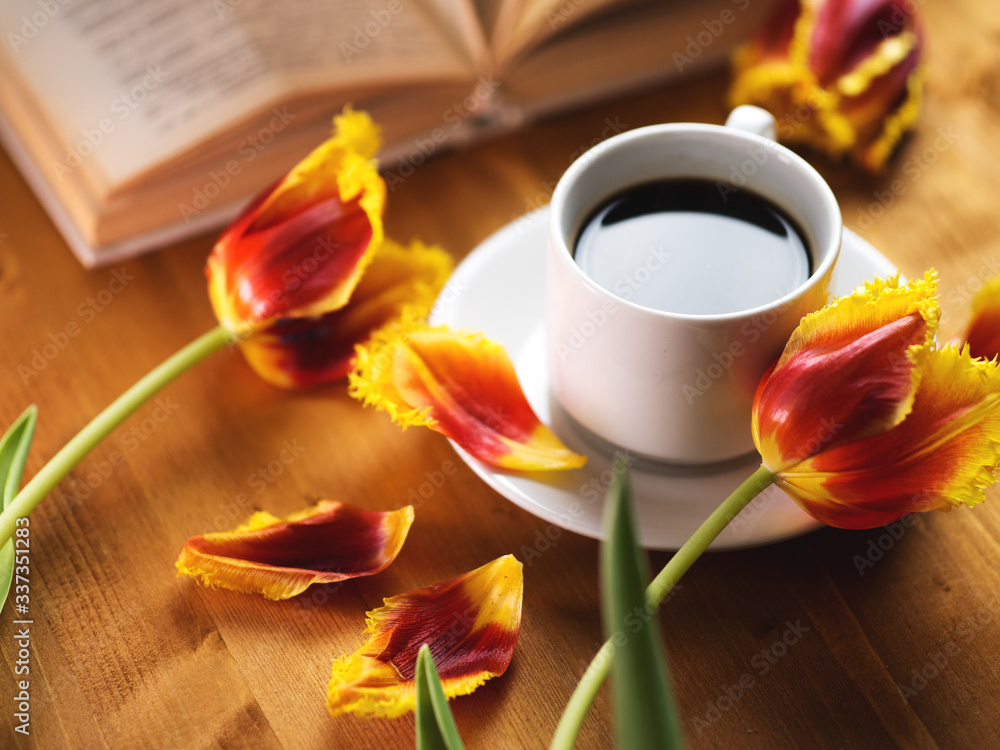 A Cup of coffee, beautiful spring tulips and a book on a natural wooden table A Cup of coffee, beautiful spring tulips and a book on a natural wooden table