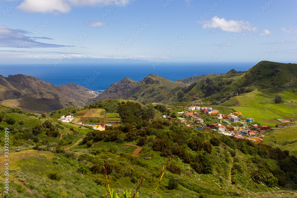 Bright green landscape of North Tenerife mountains with blue sea on background. Colorful houses village on valley in Canary Islands, Spain. Sightseeing tour, holidays travel concepts