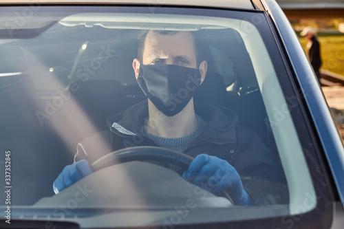 Covid-19 concept. Man drives a car in blue protective medical gloves and black face mask. Protection from bacteria and viruses. Coronavirus protection. Guarantine and corona disease.