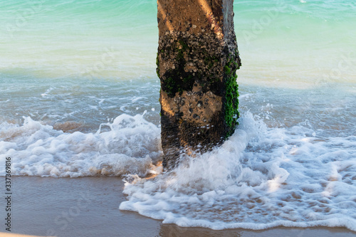 Concrete pillar with green moss and waves in the sea