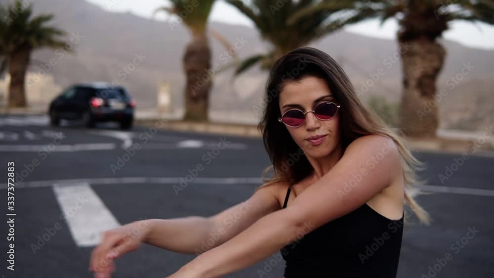 Stylish young woman in sunglasses dances in the middle of the road - slow motion - Woman in black top freerly moves her body. Relax time. Palm trees on background Stylish young woman in sunglasses dances in the middle of the road - slow motion - Woman in black top freerly moves her body. Relax time. Palm trees on background