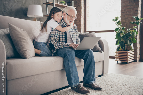 Profile photo of funny old grandpa little granddaughter sit sofa stay house quarantine safety watch movie notebook talk skype relatives modern design interior living room indoors