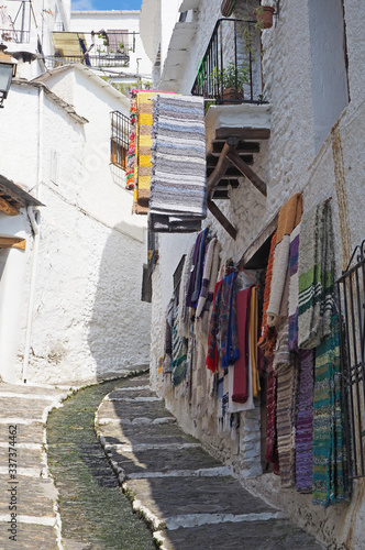 Fototapeta Naklejka Na Ścianę i Meble -  The old empty small town with low white stone houses and multicolor handmade rugs on the walls and the balcony in Europe on the sunny day