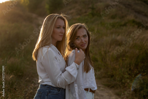 horizontal portrait of two cute adult sisters in white blouses and shorts on the background of a path in the field