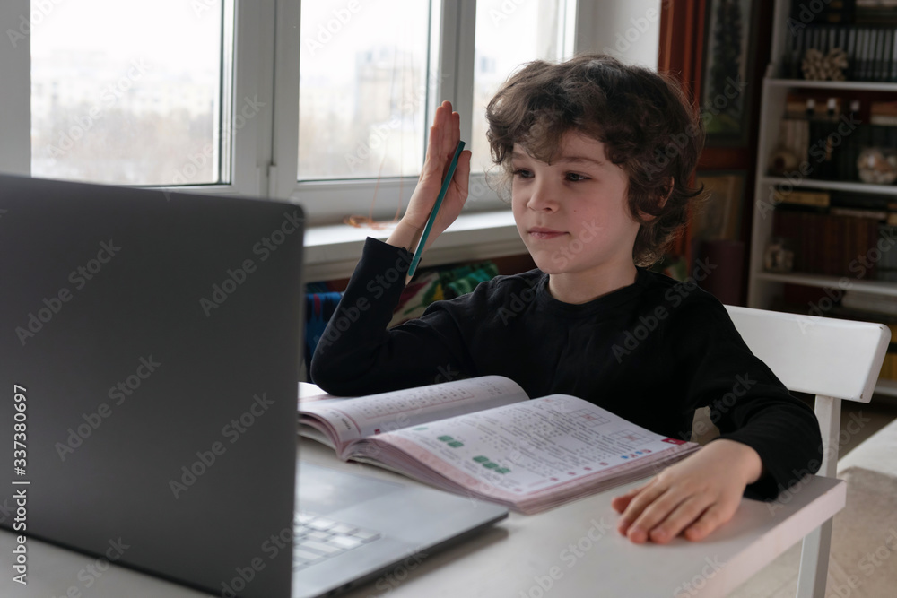 Indoor life at the coronavirus quarantine. Cute curly boy has school lesson online. Indoor life at the coronavirus quarantine. Cute curly boy has school lesson online.