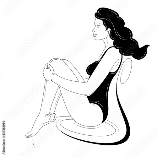 A brunette girl is sitting in a black bikini on an armchair.