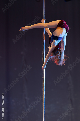 Girl athlete gymnast shows an acrobatic performance on a pylon.