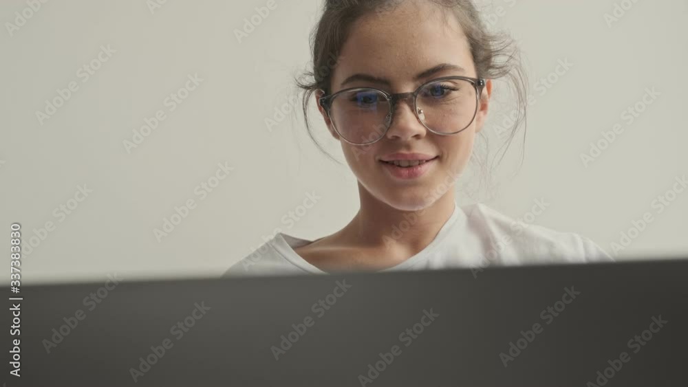 Happy pretty brunette woman in eyeglasses using laptop computer while sitting on sofa at home Happy pretty brunette woman in eyeglasses using laptop computer while sitting on sofa at home
