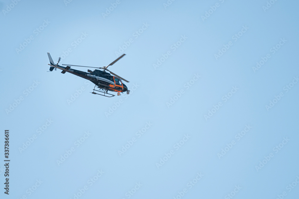 Orange and dark blue helicopter with video cameras flying with clear blue sky on background Orange and dark blue helicopter with video cameras flying with clear blue sky on background