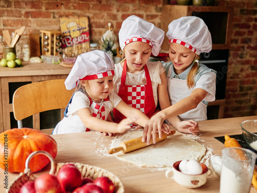 Three little chefs enjoying in the kitchen making cakes. Girls at the kitchen. Family housekeeping.