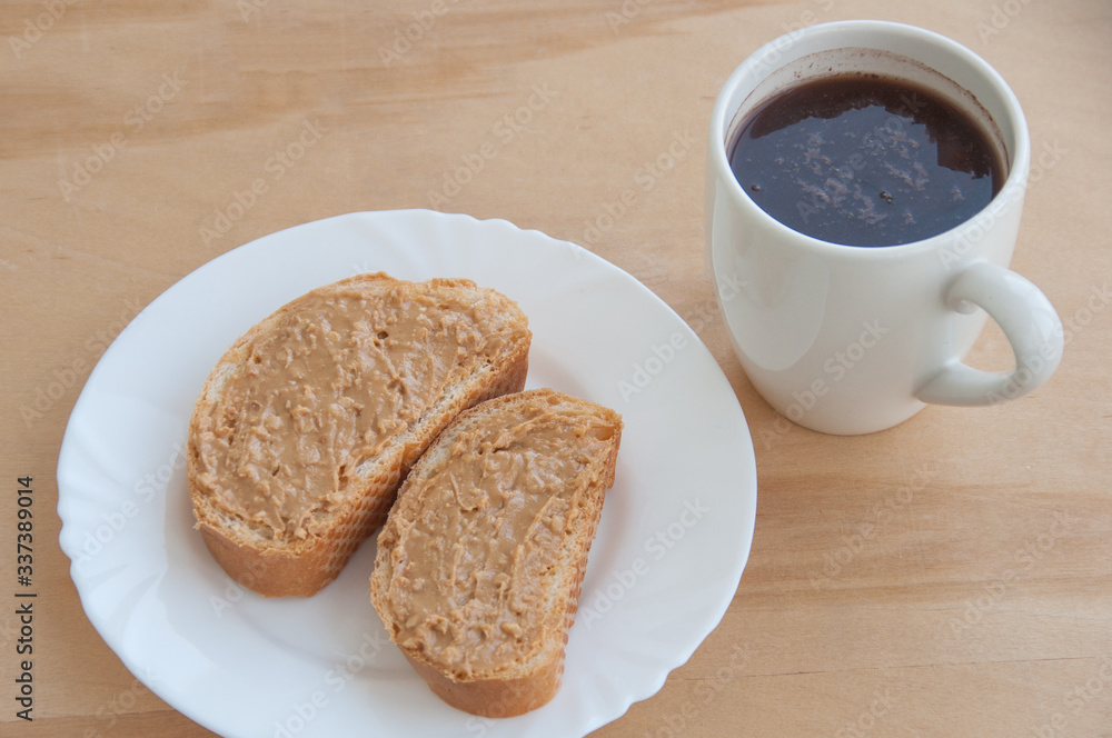 A plate with toasted bread and peanut butter, a cup of coffee on the wooden table close-up A plate with toasted bread and peanut butter, a cup of coffee on the wooden table close-up