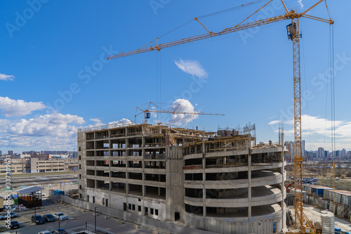 Construction crane at work on a construction site against the blue sky. Construction of a covered Parking lot.