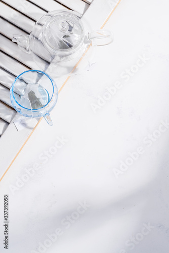 Teapot and glass on a white background with part of wooden jalousie. Top view.
