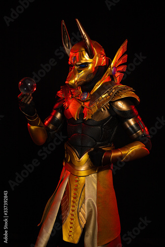 a male actor in a suit of an Egyptian mythology character, the golden deity Jackal Anubis, twists buugeng in red light on a black background photo