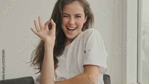 Happy pretty brunette woman showing ok sign and looking at the camera at home photo