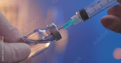 Syringe with needle filling with transparent fluid. Vial filled with vaccine or other medicine. Close-up shot on laboratory background. photo