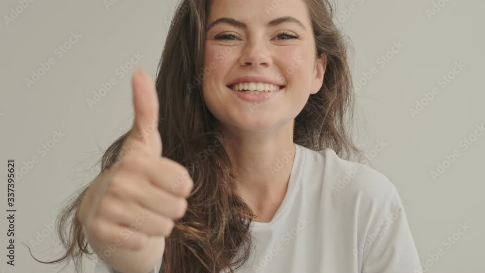 Cheerful pretty brunette woman showing thumb up and looking at the camera at home Cheerful pretty brunette woman showing thumb up and looking at the camera at home