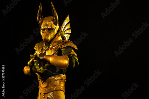 a male actor in a suit of an Egyptian mythology character, the golden deity Jackal Anubis, twists buugeng in yellow light on a black background photo