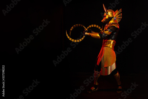 a male actor in a suit of an Egyptian mythology character, the golden deity Jackal Anubis, twists buugeng in red light on a black background photo